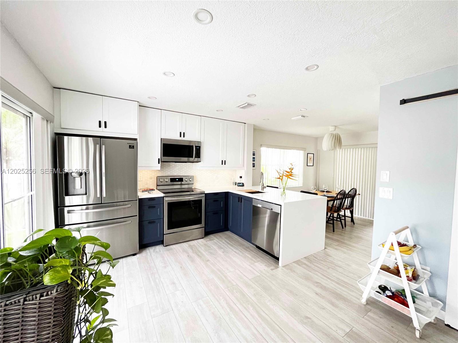 A modern kitchen features white upper cabinets, dark blue lower cabinets, and a white island — 9832 NW 9th Ct, Plantation FL 33324, PLANTATION, FL