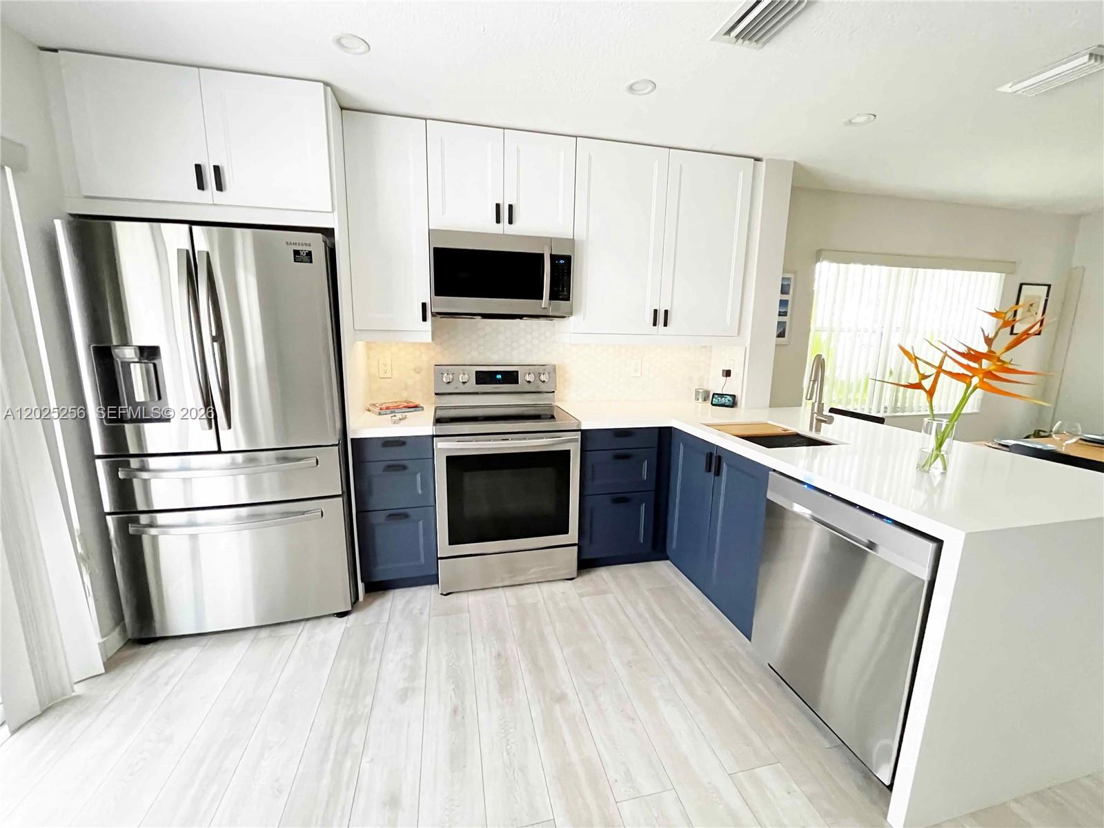A modern kitchen features white upper cabinets, blue lower cabinets, stainless steel appliances, and countertops — 9832 NW 9th Ct, Plantation FL 33324, PLANTATION, FL