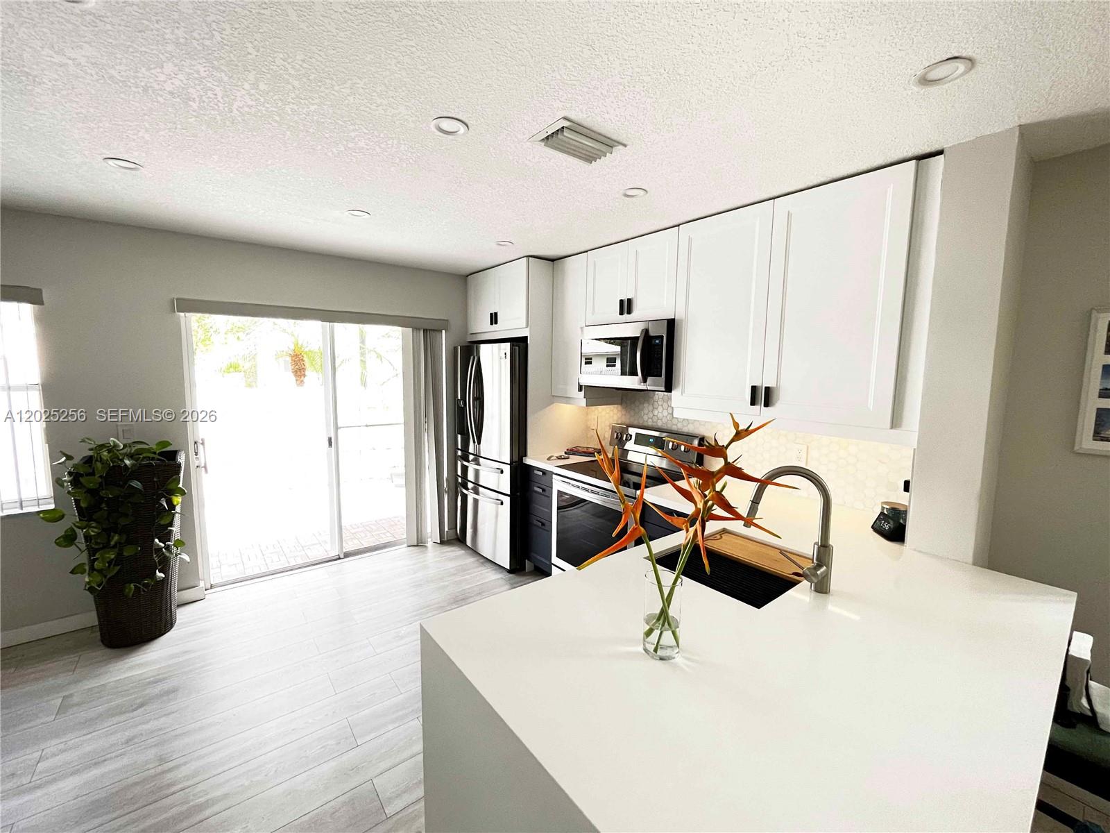 A modern kitchen features white upper cabinets, dark lower cabinets, and a white quartz island — 9832 NW 9th Ct, Plantation FL 33324, PLANTATION, FL