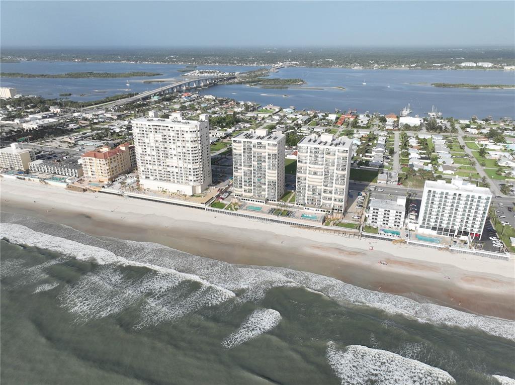 An aerial view shows several high-rise beachfront condominiums along a sandy coastline near a bridge — 3315 S ATLANTIC AVENUE UNIT 806, DAYTONA BEACH SHORES, FL