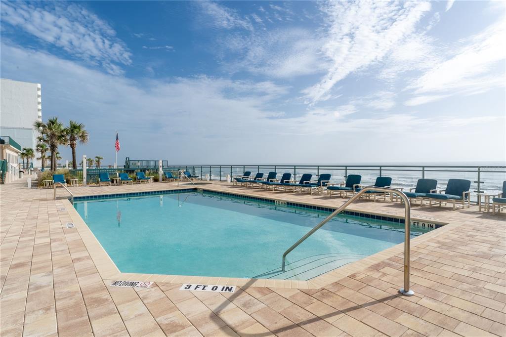 An outdoor swimming pool with lounge chairs overlooks the ocean on a sunny day — 3315 S ATLANTIC AVENUE UNIT 806, DAYTONA BEACH SHORES, FL
