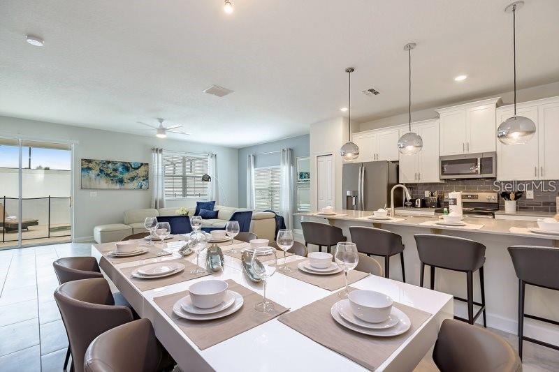 A modern open-concept dining area and kitchen featuring a long white table and pendant lighting — 1585 SANDBAGGER DRIVE, CHAMPIONS GATE, FL