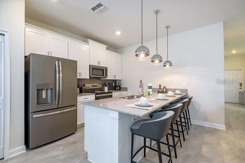 A modern kitchen features white cabinetry, stainless steel appliances, and a large quartz-topped island — 1585 SANDBAGGER DRIVE, CHAMPIONS GATE, FL