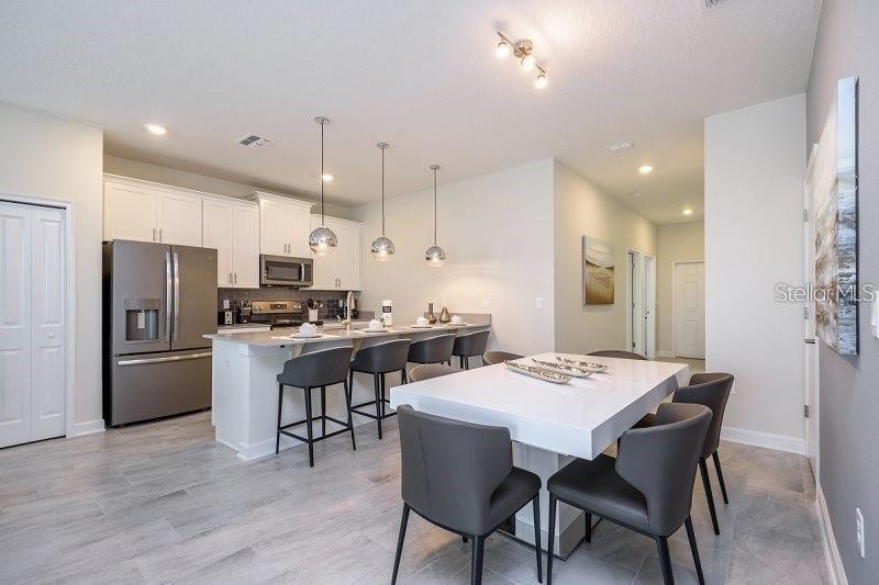 A modern kitchen with white cabinets, a central island, and an adjacent dining table — 1585 SANDBAGGER DRIVE, CHAMPIONS GATE, FL