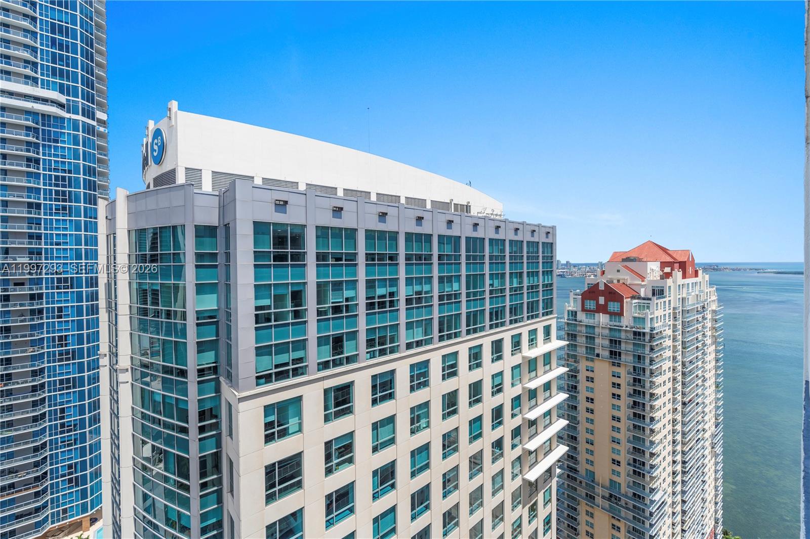An exterior view of high-rise apartment buildings overlooking the ocean under a clear blue sky — 1200 Brickell Bay Dr # 4218, Miami FL 33131, MIAMI, FL