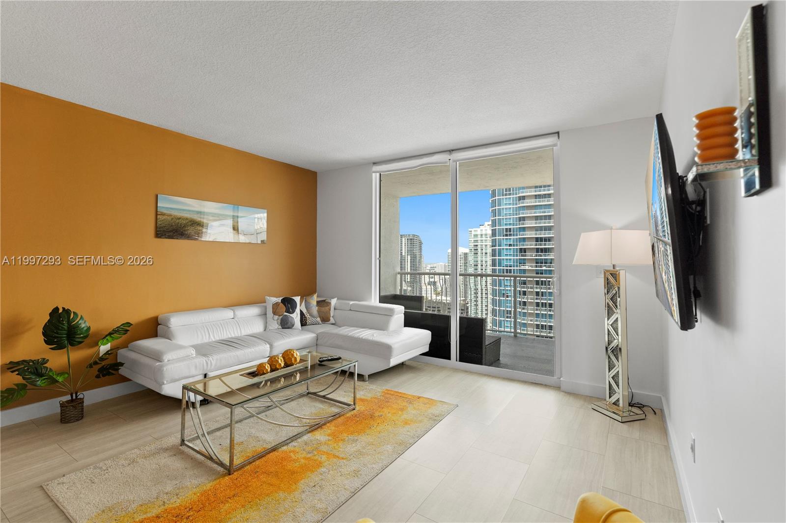 A living room features a white sectional sofa, orange accent wall, and balcony with city views — 1200 Brickell Bay Dr # 4218, Miami FL 33131, MIAMI, FL