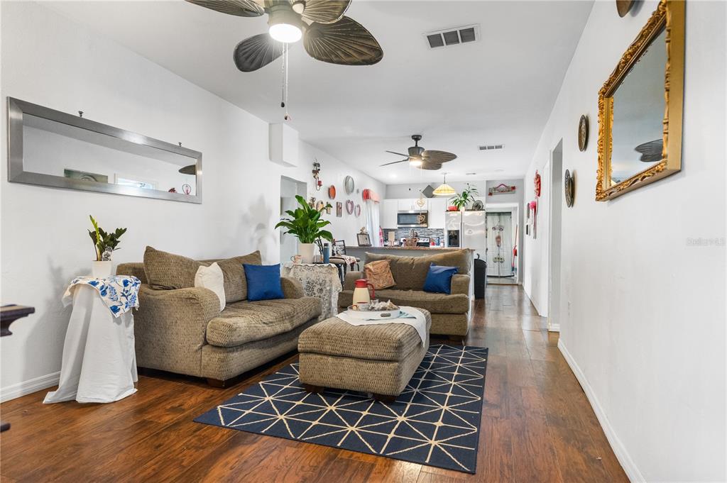 A living room with brown sofas, a patterned rug, and an open kitchen beyond — 221 AVENUE L NE, WINTER HAVEN, FL