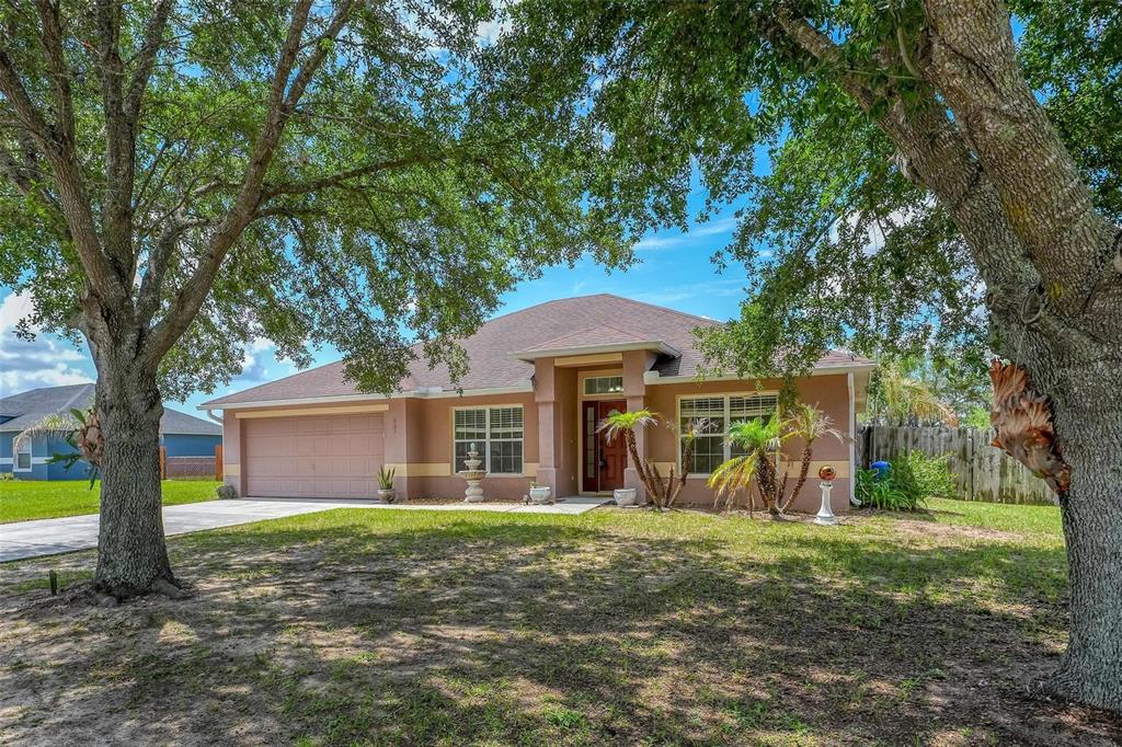 A single-story tan house with a two-car garage sits behind two large oak trees — 537 HATCHWOOD DRIVE, HAINES CITY, FL