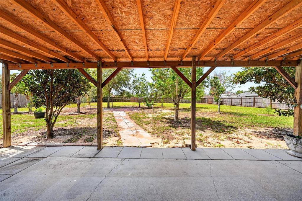 A covered concrete patio overlooks a grassy backyard with trees and a stone walkway — 537 HATCHWOOD DRIVE, HAINES CITY, FL
