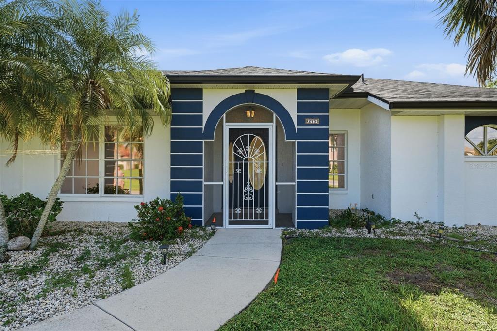 A single-story house with a white stucco exterior, blue arched entryway, and a palm tree — 275 ROTONDA BOULEVARD N, ROTONDA WEST, FL