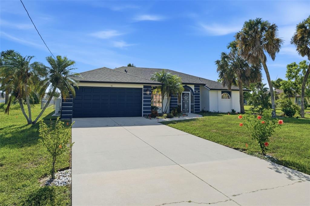 A single-story house with a dark garage door, white stucco walls, and palm trees — 275 ROTONDA BOULEVARD N, ROTONDA WEST, FL