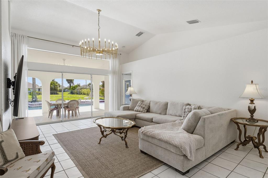 A living room features a sectional sofa, a chandelier, and sliding doors opening to a pool — 275 ROTONDA BOULEVARD N, ROTONDA WEST, FL