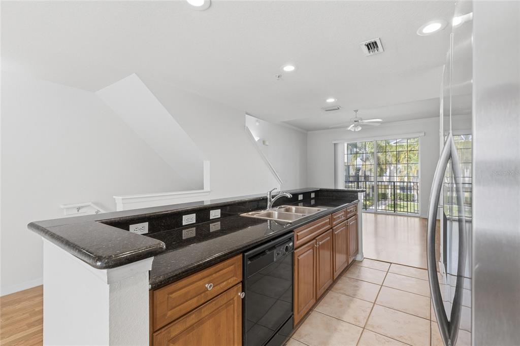A kitchen with wood cabinets, black countertops, and a dishwasher overlooks a living area — 9875 MEADOW FIELD CIRCLE, TAMPA, FL