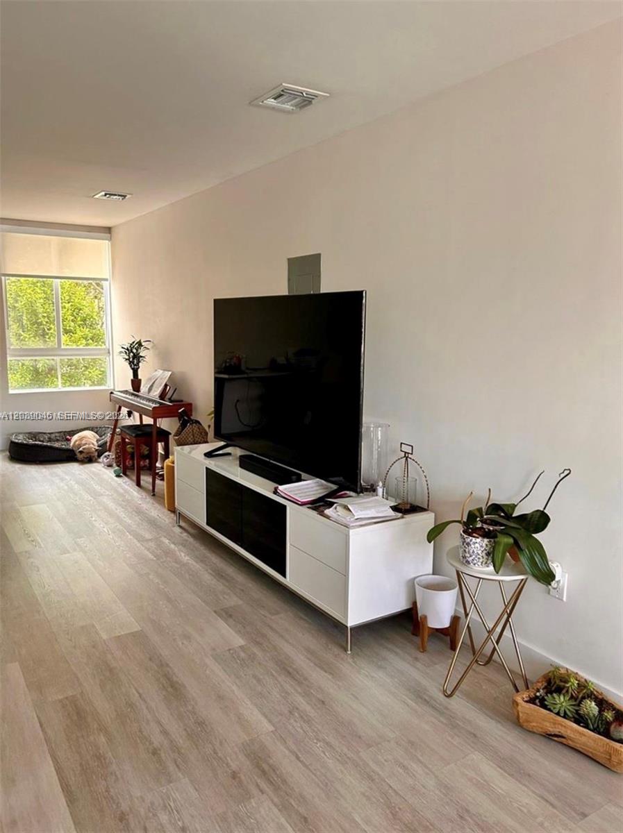 A living room features light wood-look flooring, a white media console, and a large television — 2561 NE 193rd St # 1201, Miami FL 33180, MIAMI, FL