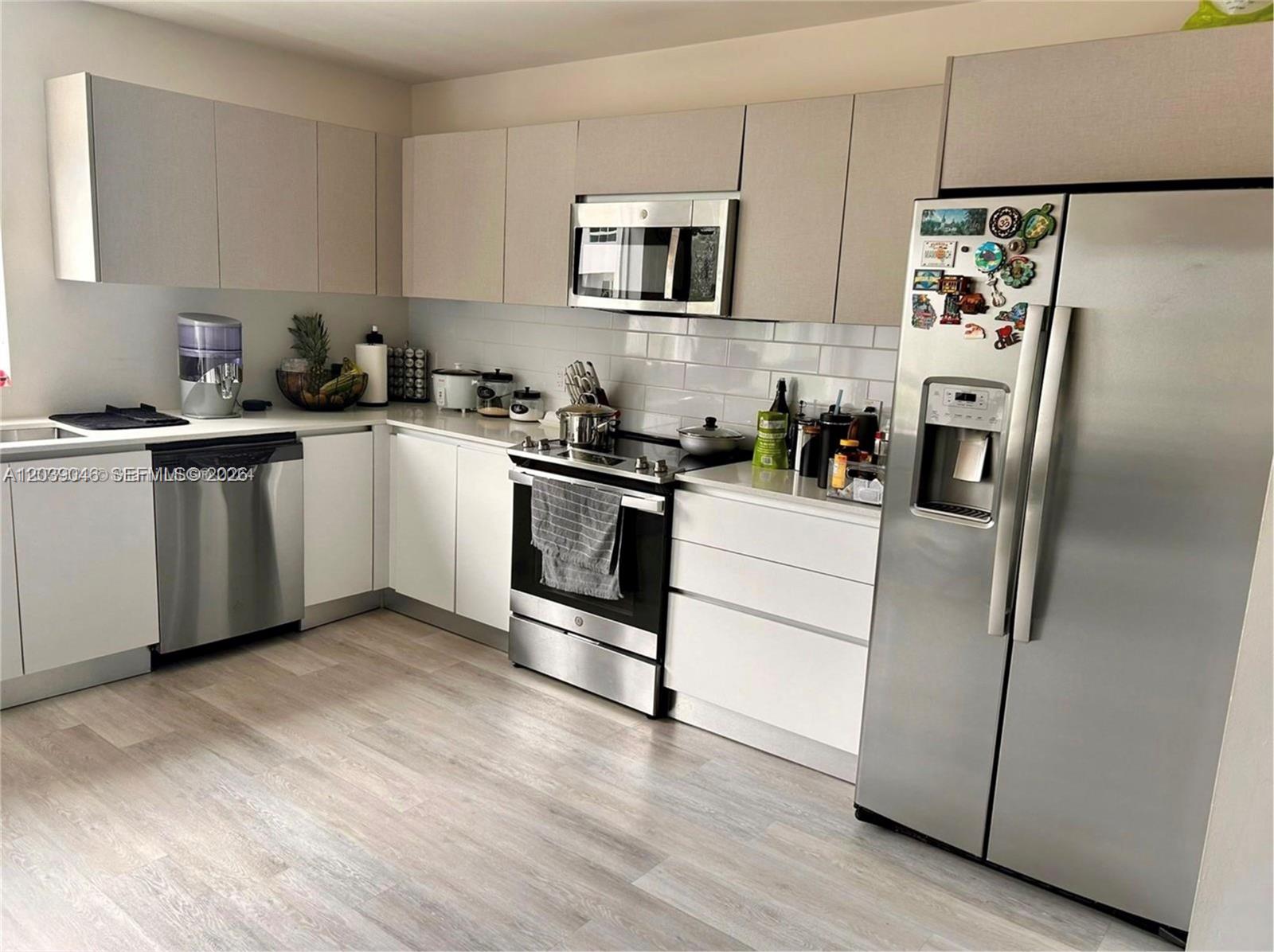 A modern kitchen features white cabinetry, stainless steel appliances, and light wood-look flooring — 2561 NE 193rd St # 1201, Miami FL 33180, MIAMI, FL