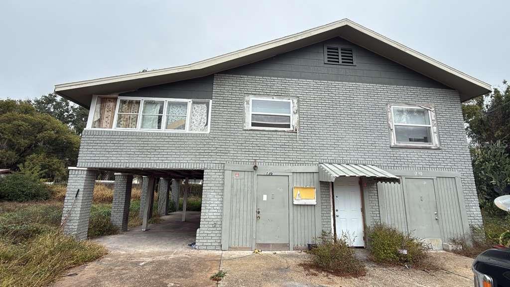 A two-story house with gray brick siding, an elevated carport, and multiple exterior doors — 730 VIRGINIA AVENUE, AUBURNDALE, FL