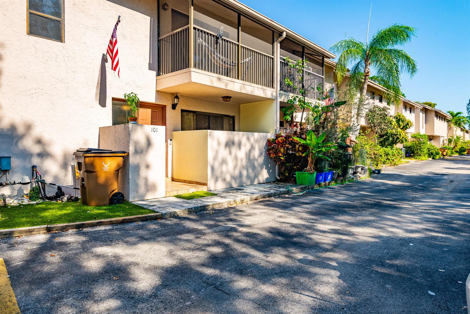 A two-story apartment building exterior features a ground-level entrance, a screened balcony, and a trash bin — 740 SE 1st Way # 101, Deerfield Beach FL 33441, DEERFIELD BEACH, FL