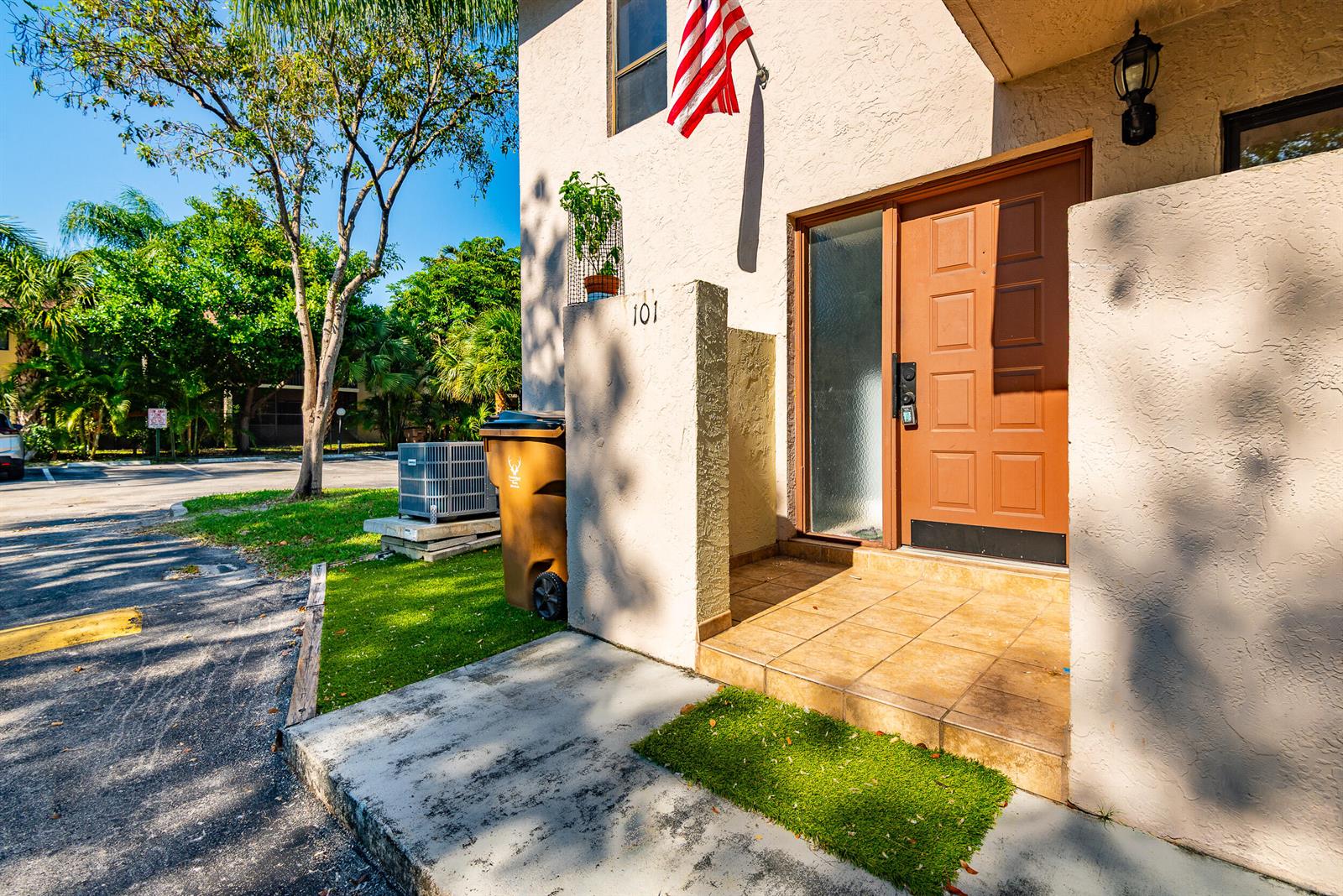 An exterior view of a residential unit entrance with a brown door and tile porch — 740 SE 1st Way # 101, Deerfield Beach FL 33441, DEERFIELD BEACH, FL