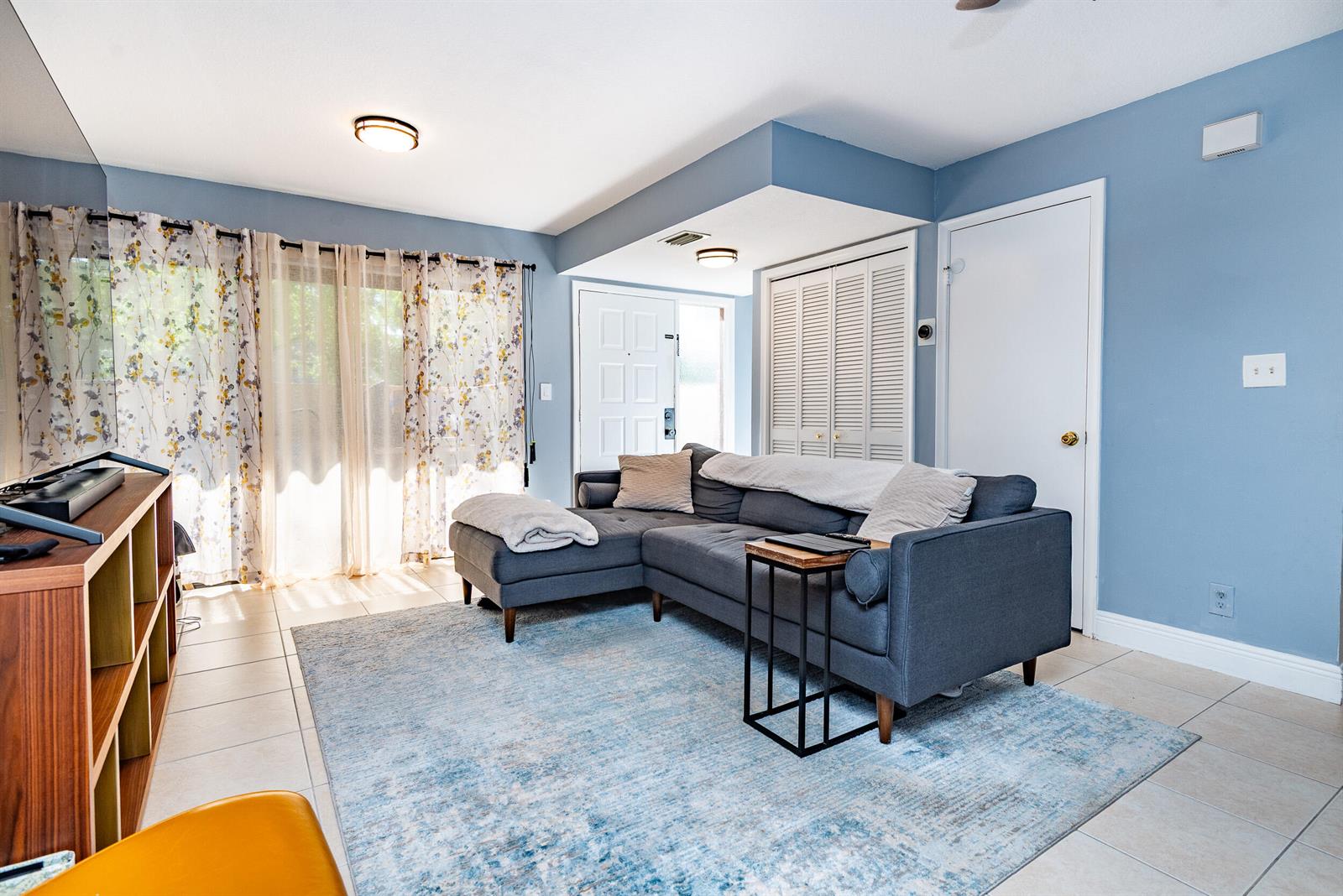 A living room features a blue sectional sofa, a patterned area rug, and tile flooring — 740 SE 1st Way # 101, Deerfield Beach FL 33441, DEERFIELD BEACH, FL