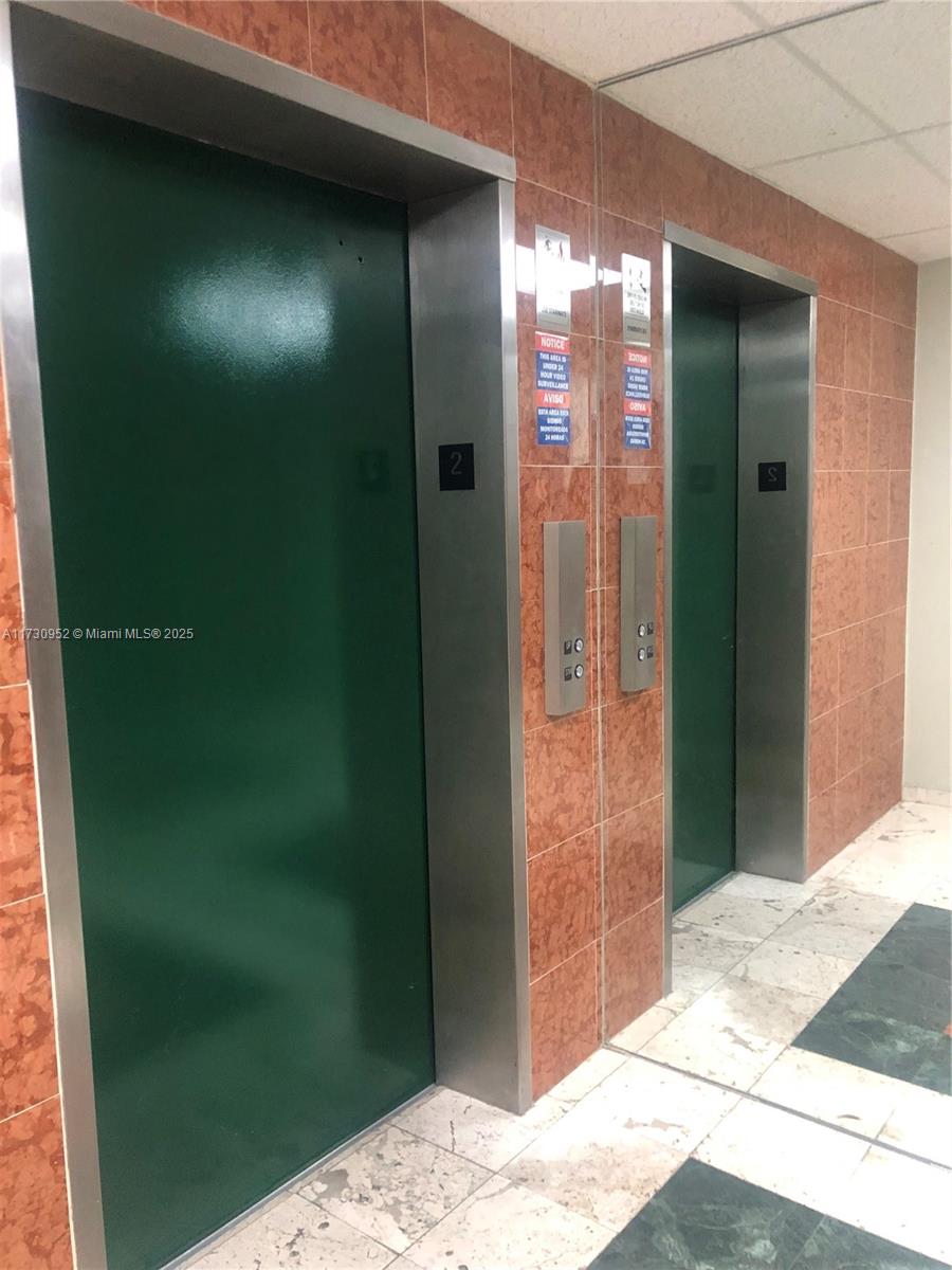Two green elevator doors are set into a wall covered in reddish-brown square tiles — 1385 SW 22 # 203, Coral Gables FL 33145, CORAL GABLES, FL