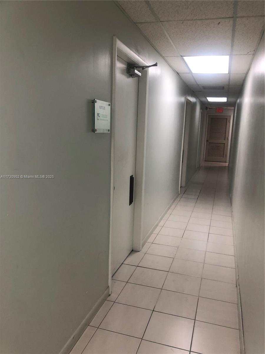 A narrow hallway features white tiled floors, light-colored walls, and a closed door with signage — 1385 SW 22 # 203, Coral Gables FL 33145, CORAL GABLES, FL