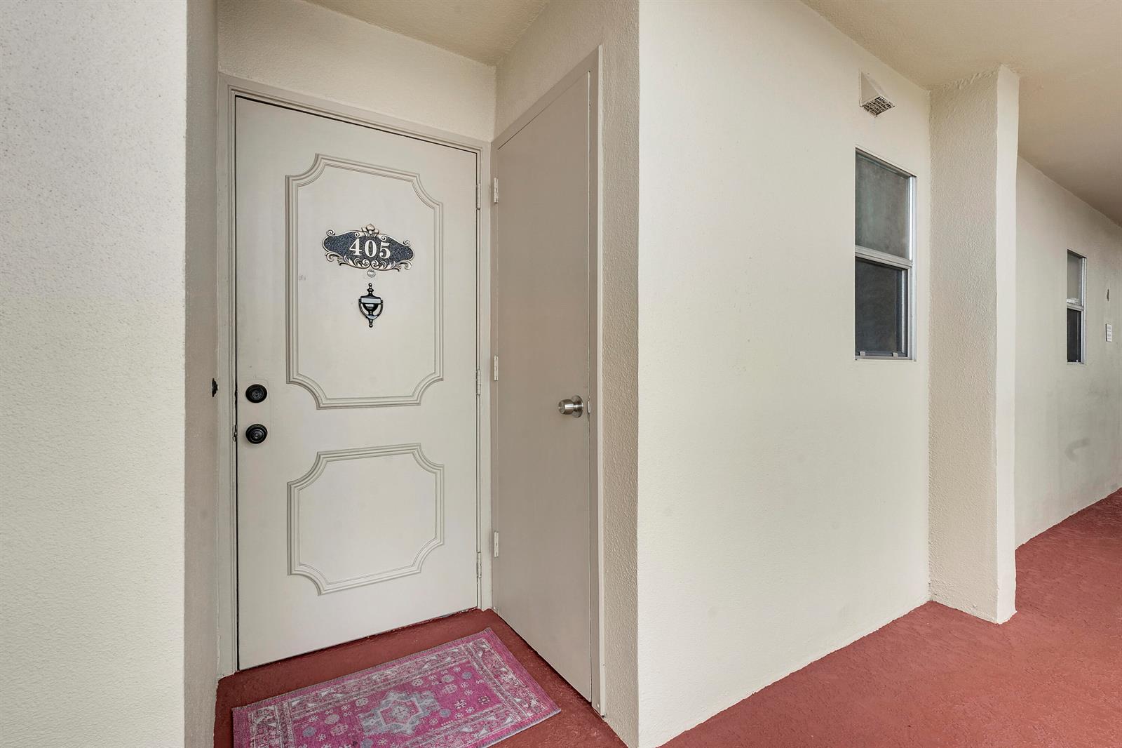 An apartment entrance with a white door numbered 405, a small closet door, and red flooring — 3755 Via Poinciana, FL 33467, FL