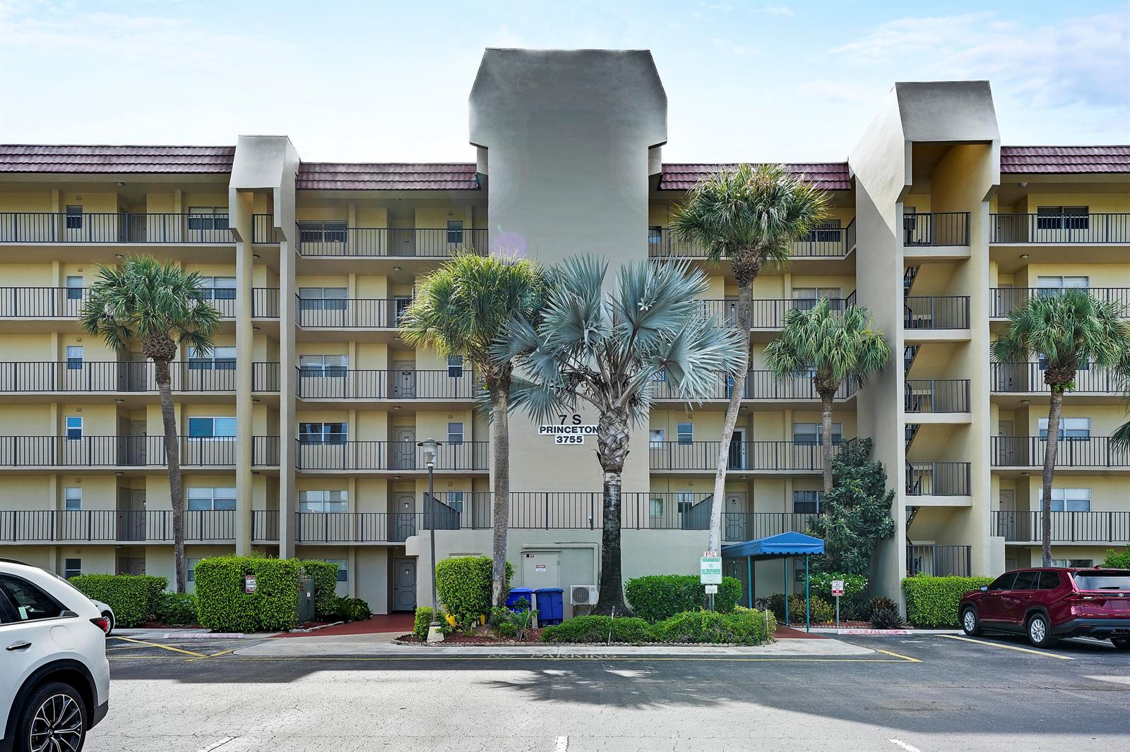 A multi-story apartment building features balconies, palm trees, and a parking lot in front — 3755 Via Poinciana, FL 33467, FL