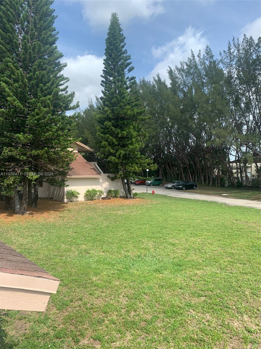 A grassy lawn sits in front of a building with tall pine trees — 300 Nottingham Cir # J, Green Acres FL 33463, GREEN ACRES, FL
