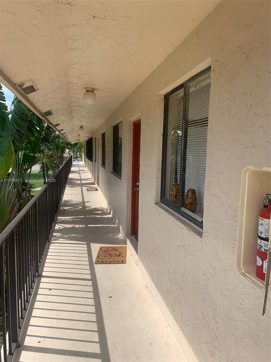 An outdoor walkway with a metal railing, beige walls, and a fire extinguisher cabinet — 300 Nottingham Cir # J, Green Acres FL 33463, GREEN ACRES, FL