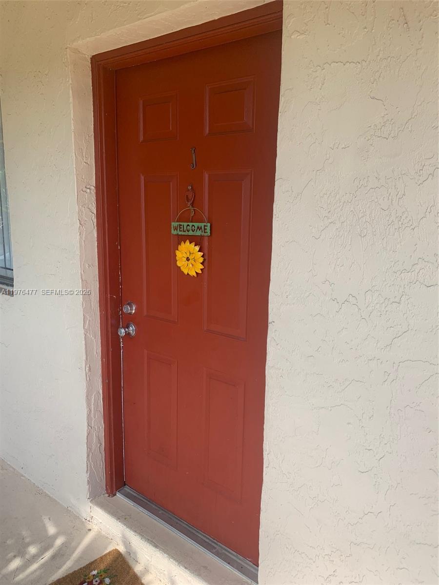 A red front door with a sunflower welcome sign is set in a beige wall — 300 Nottingham Cir # J, Green Acres FL 33463, GREEN ACRES, FL