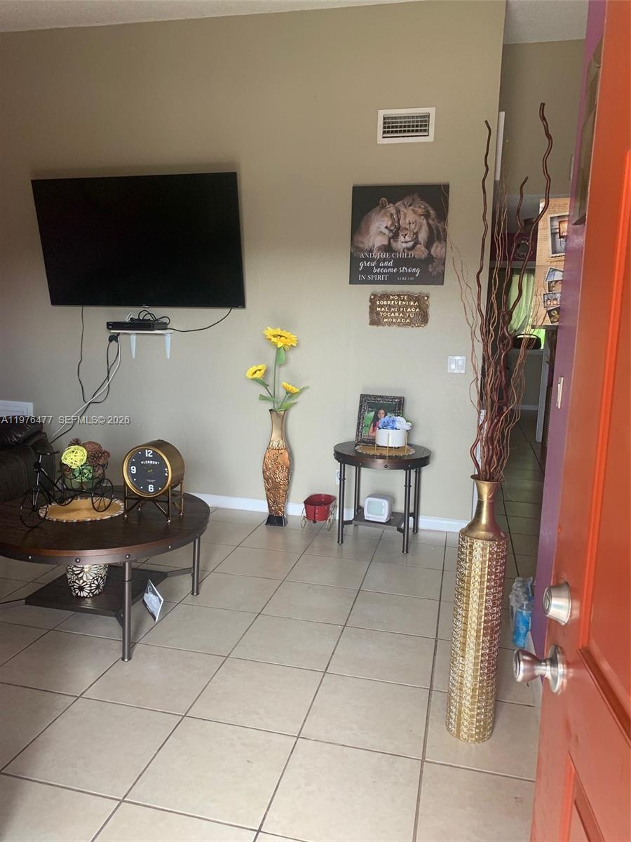 A living room features a wall-mounted television, a round coffee table, and decorative floor vases — 300 Nottingham Cir # J, Green Acres FL 33463, GREEN ACRES, FL