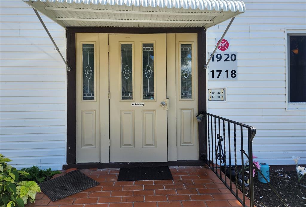 A beige front door with glass panels sits under a metal awning on a brick porch — 22481 WESTCHESTER BOULEVARD UNIT A19, PUNTA GORDA, FL