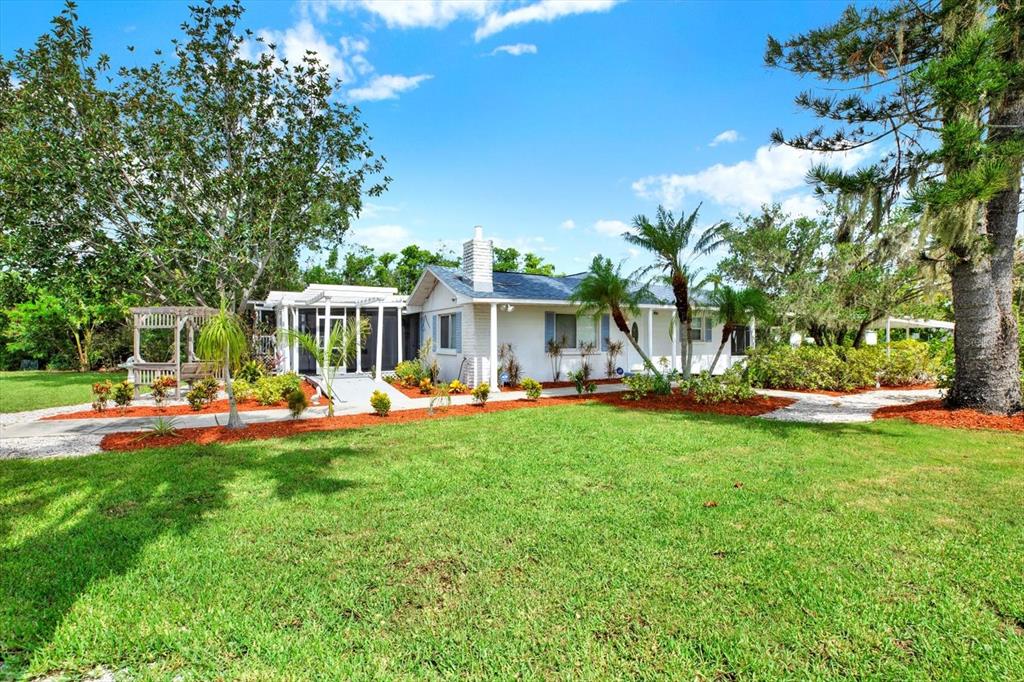 A white single-story house with a screened porch and red mulch landscaping under a blue sky — 102 W NORTH BRANCH ROAD, RUSKIN, FL