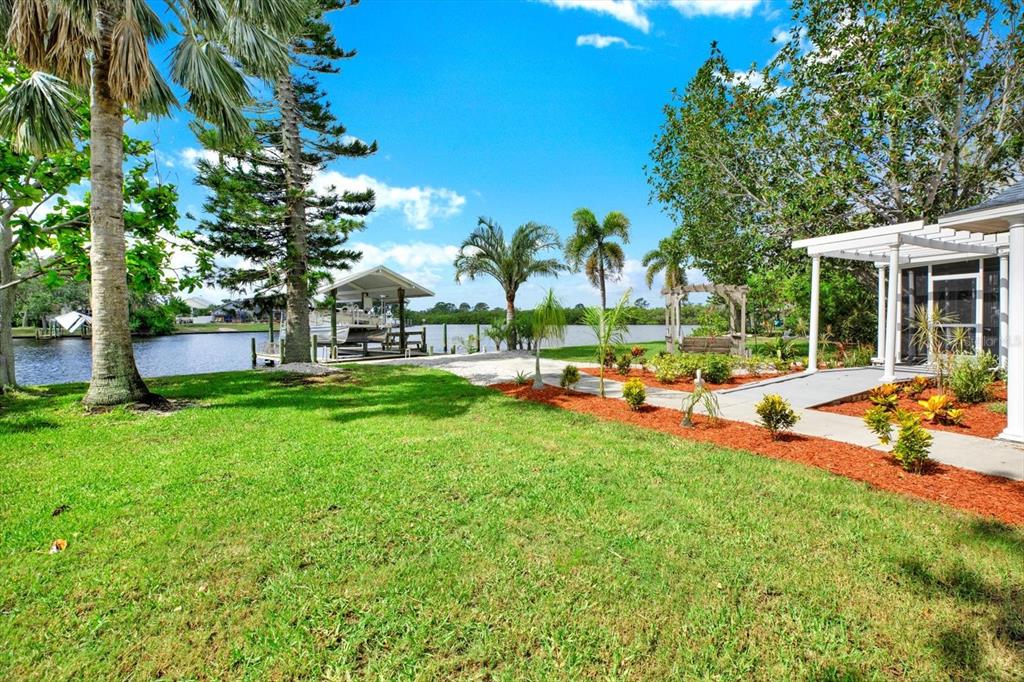 A grassy backyard features a boat dock, palm trees, and a pergola-covered patio by water — 102 W NORTH BRANCH ROAD, RUSKIN, FL