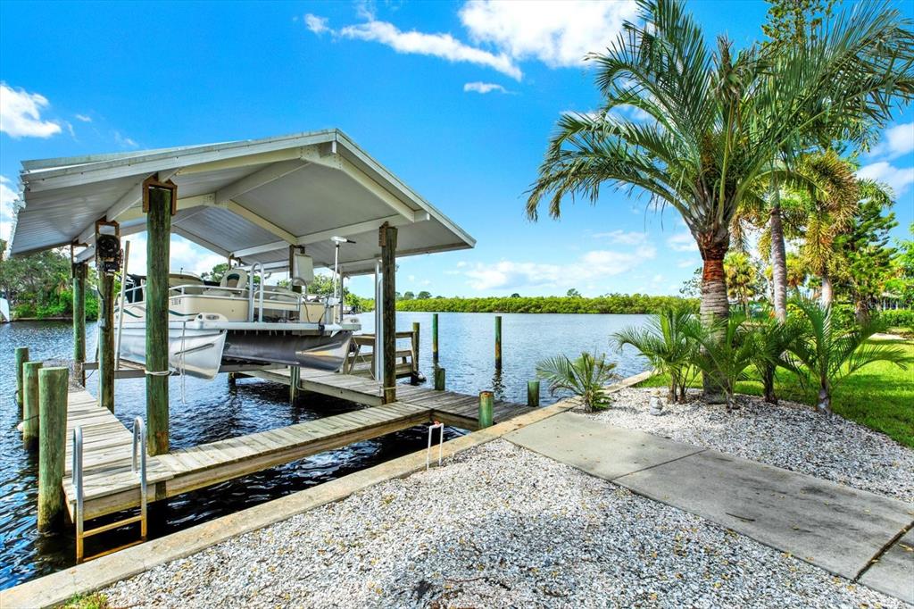 A boat lift with a pontoon boat sits beside a wooden dock and palm trees — 102 W NORTH BRANCH ROAD, RUSKIN, FL