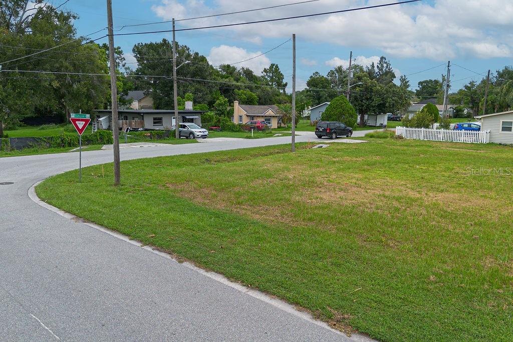 A grassy vacant lot sits at a street corner with a yield sign and houses — 5102 SUNRISE BOULEVARD, ORLANDO, FL