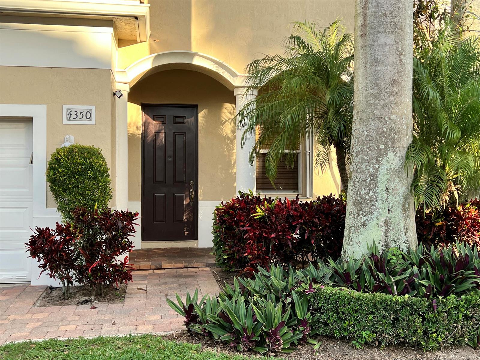 A tan house exterior features a dark brown front door, arched entryway, and landscaped garden — 4350 Key Lime Boulevard, Boynton Beach FL 33436, BOYNTON BEACH, FL