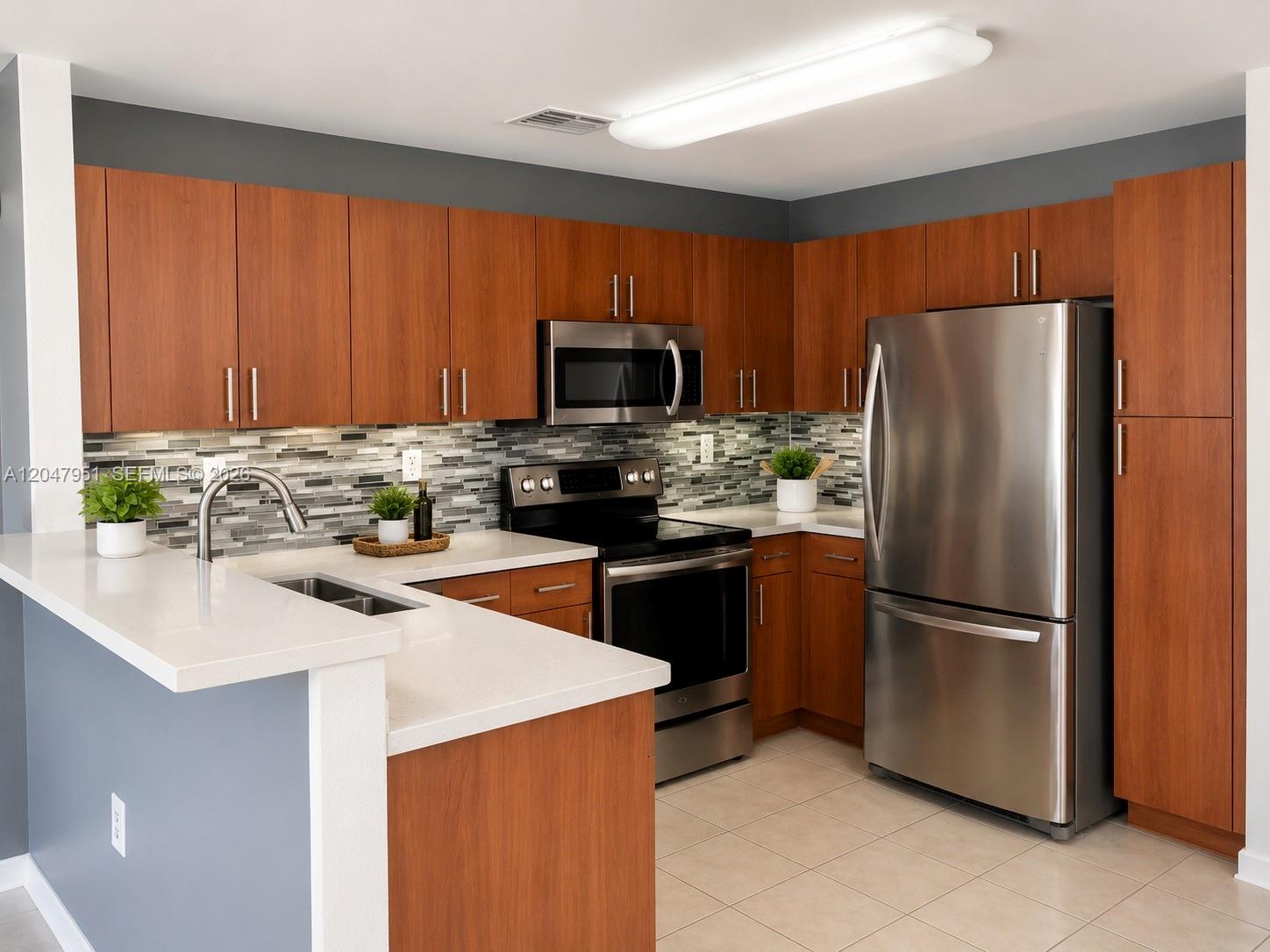 A kitchen features wood cabinets, stainless steel appliances, a tiled backsplash, and white countertops — 3092 SW 129th Ter # 102, Miramar FL 33027, MIRAMAR, FL