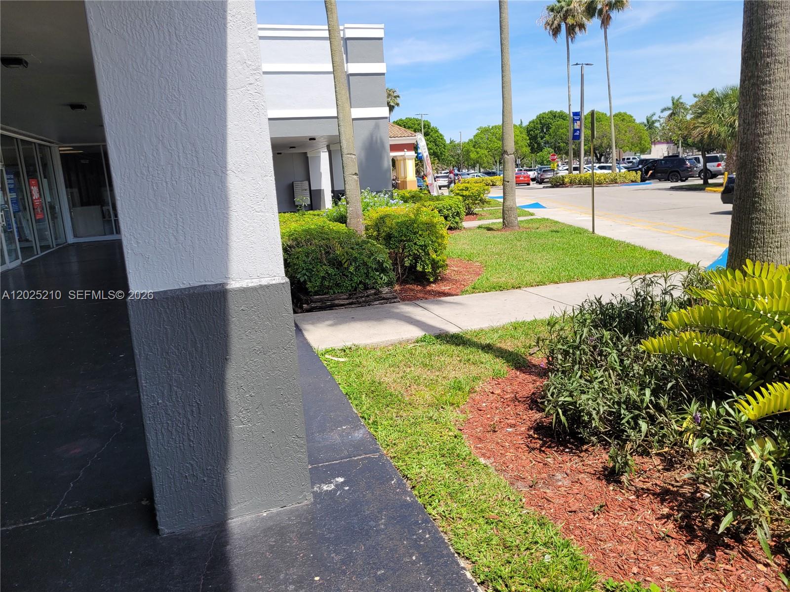 A view of a building exterior with a covered walkway, landscaping, and a parking lot — 6935 Taft, Hollywood FL 33125, HOLLYWOOD, FL