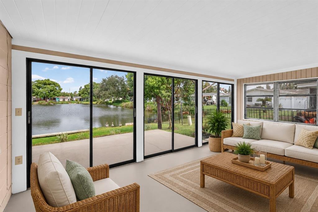 A sunroom with sliding glass doors overlooking a lake, wicker furniture, and a beige rug — 2044 PAMELA DRIVE, HOLIDAY, FL