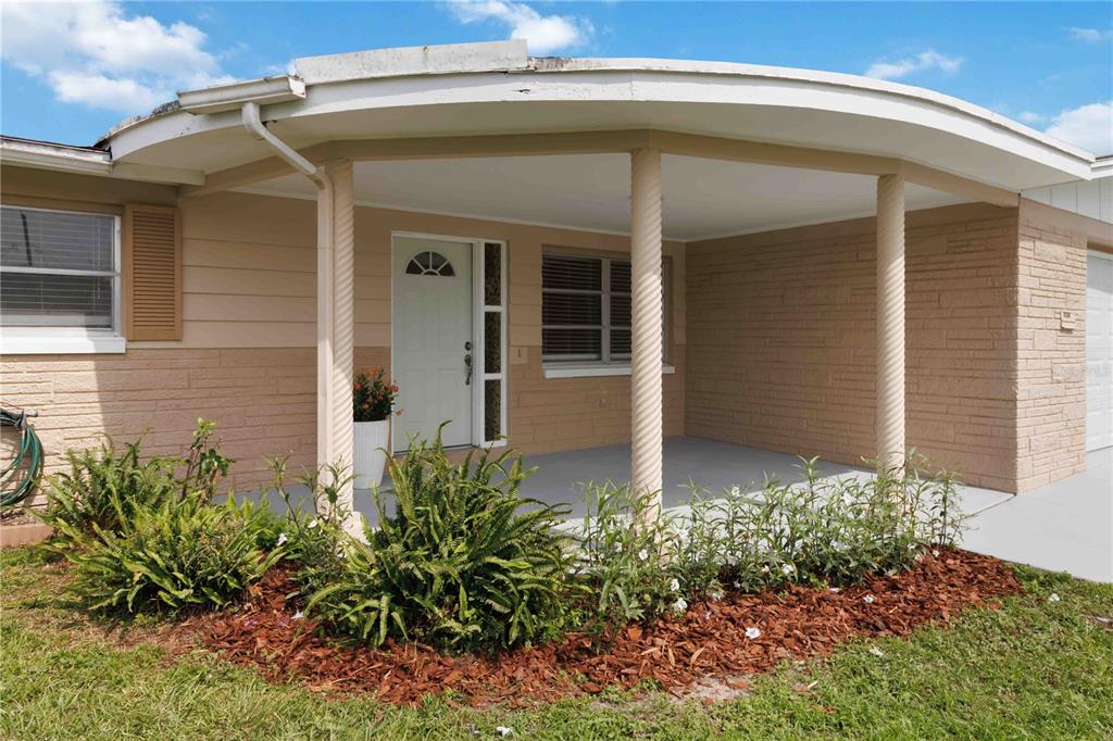 A single-story house exterior features a curved covered porch with three spiral columns and landscaping — 2044 PAMELA DRIVE, HOLIDAY, FL