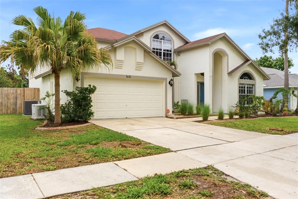 A two-story house with a beige stucco exterior, a two-car garage, and a palm tree — 1610 LEDGESTONE DRIVE, BRANDON, FL