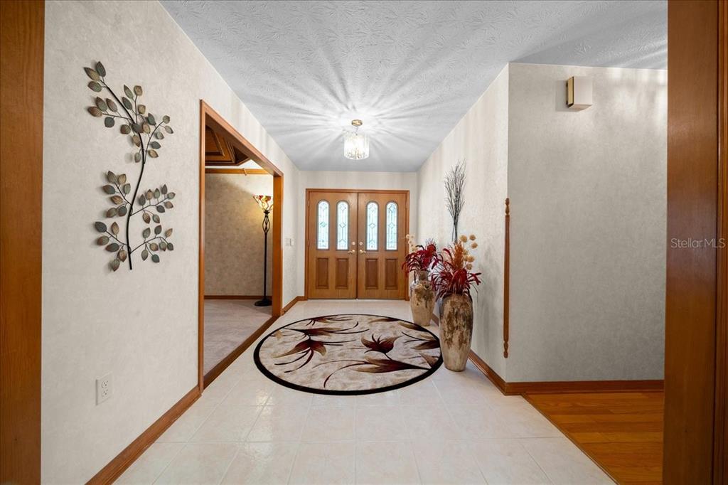 A foyer features a tiled floor, a round rug, double wooden doors, and wall decor — 11 SYCAMORE COURT W, HOMOSASSA, FL