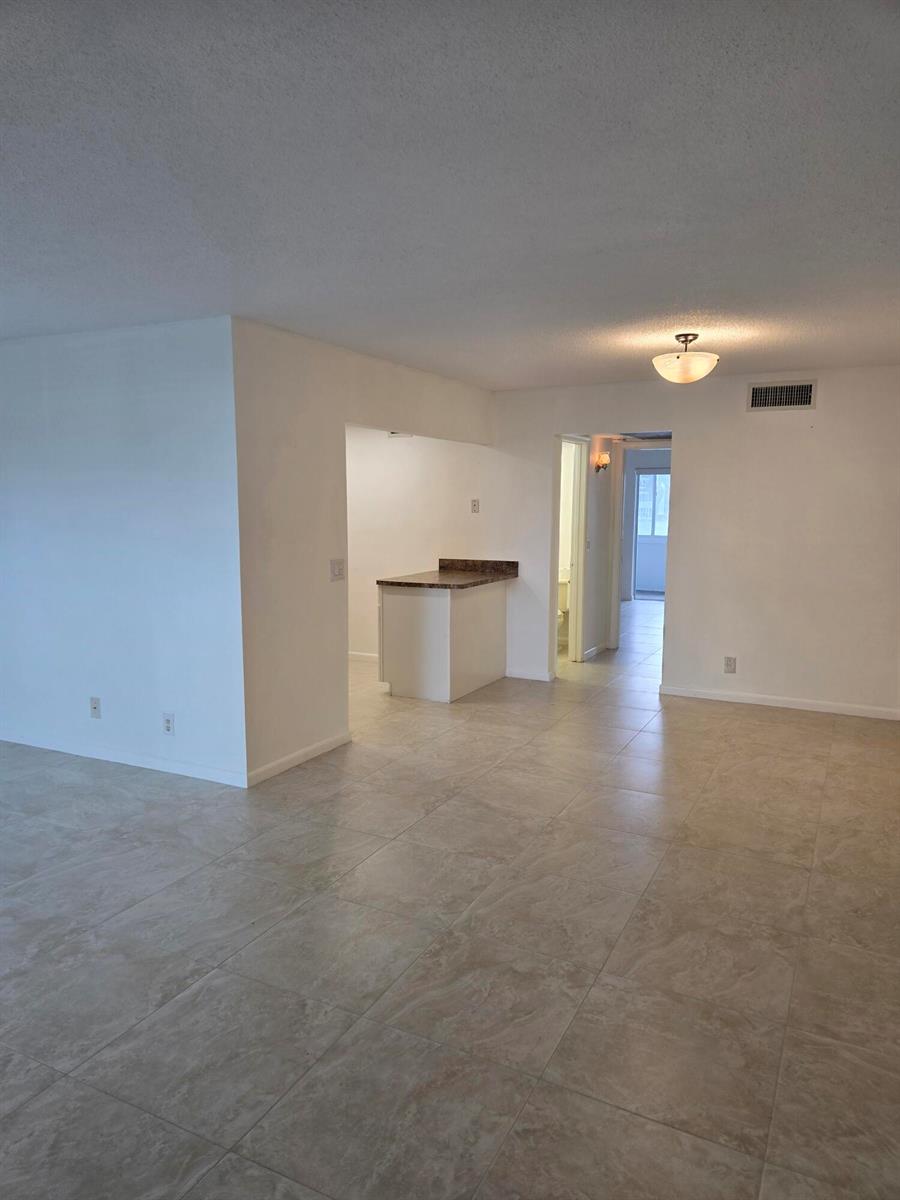 An open-concept living area features light-colored tile flooring, white walls, and a kitchen peninsula — WEST PALM BEACH, FL