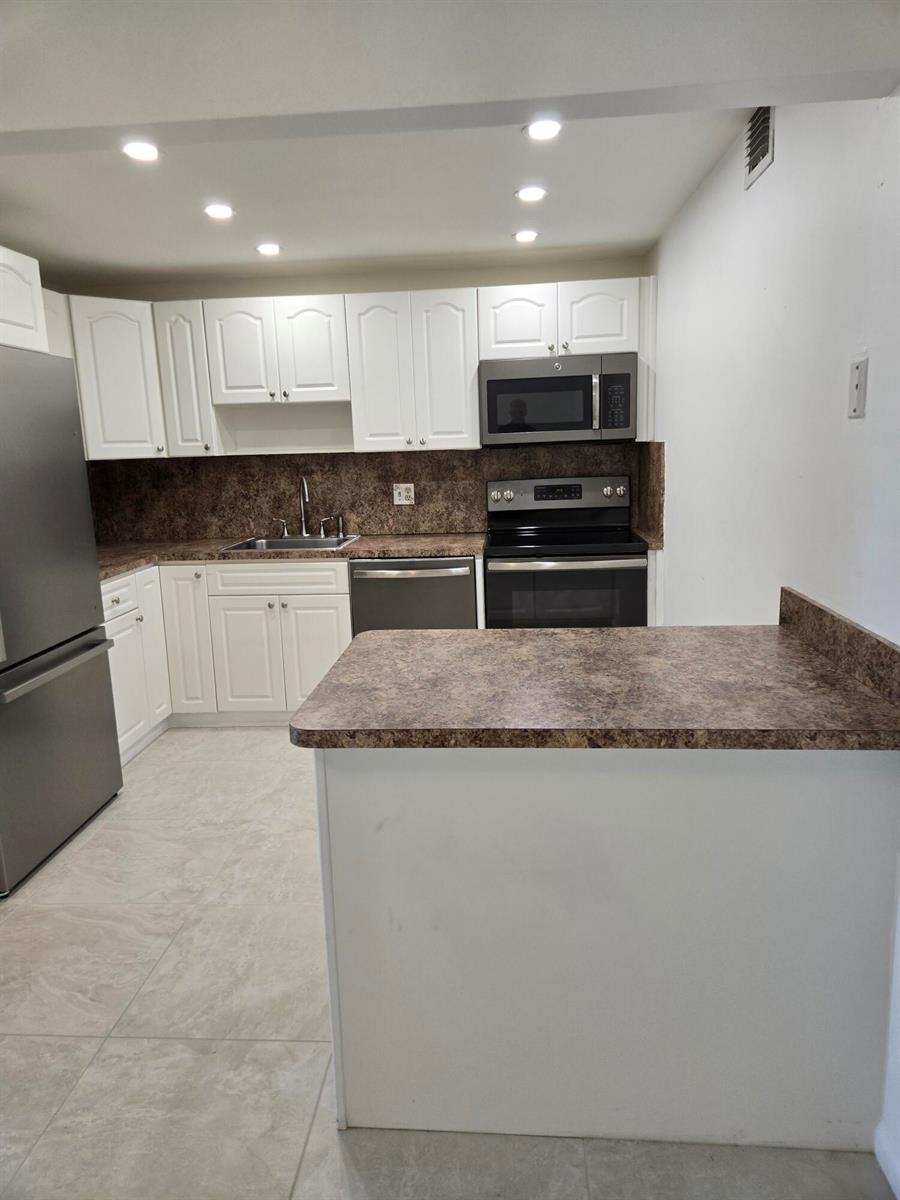 A kitchen features white cabinets, dark brown countertops, stainless steel appliances, and light tile flooring — WEST PALM BEACH, FL