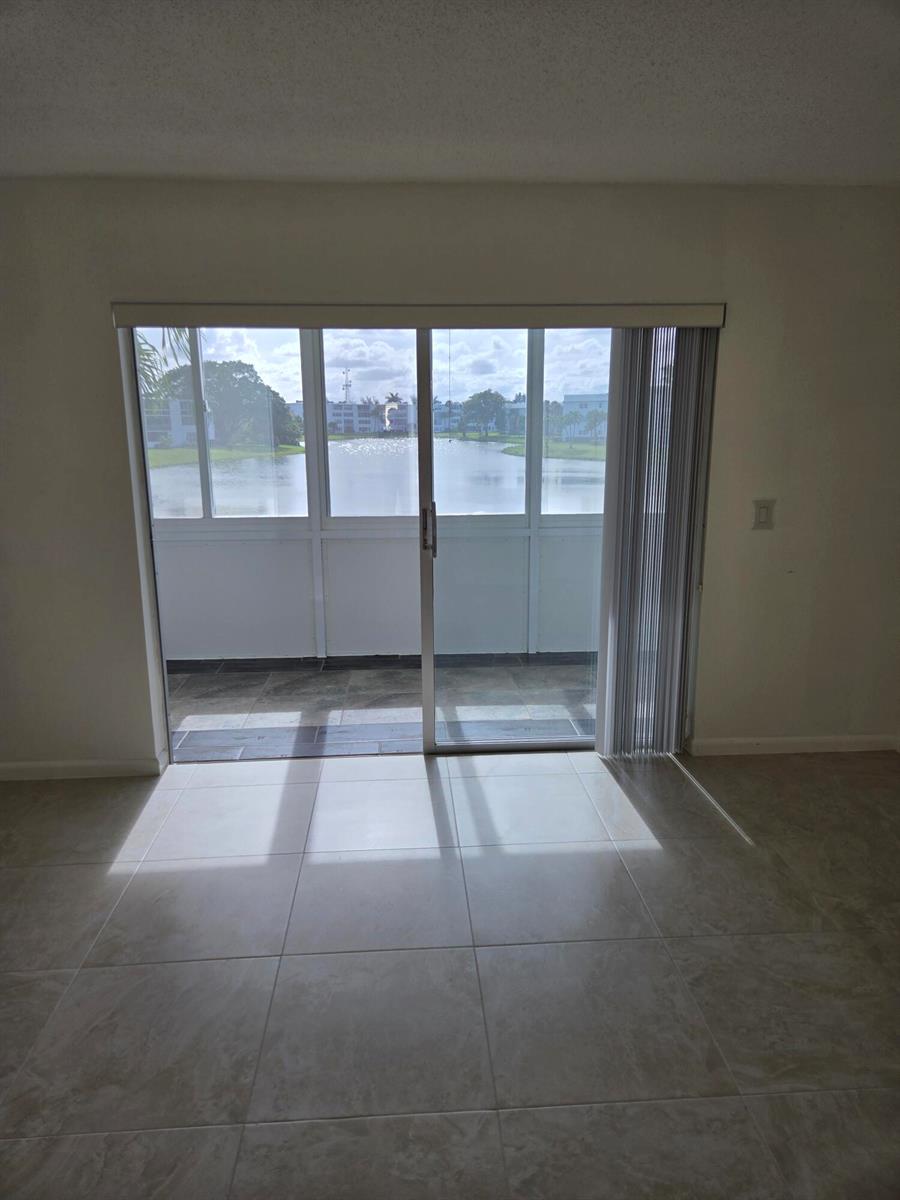 A room with light-colored tile flooring features a sliding glass door opening to a balcony — WEST PALM BEACH, FL