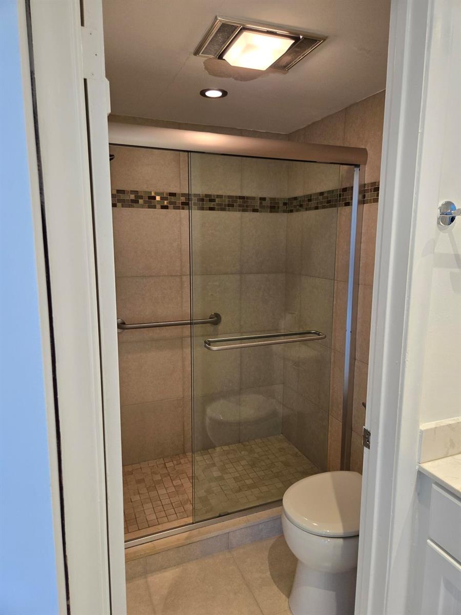 A bathroom featuring a tiled walk-in shower with a glass door and a toilet — WEST PALM BEACH, FL
