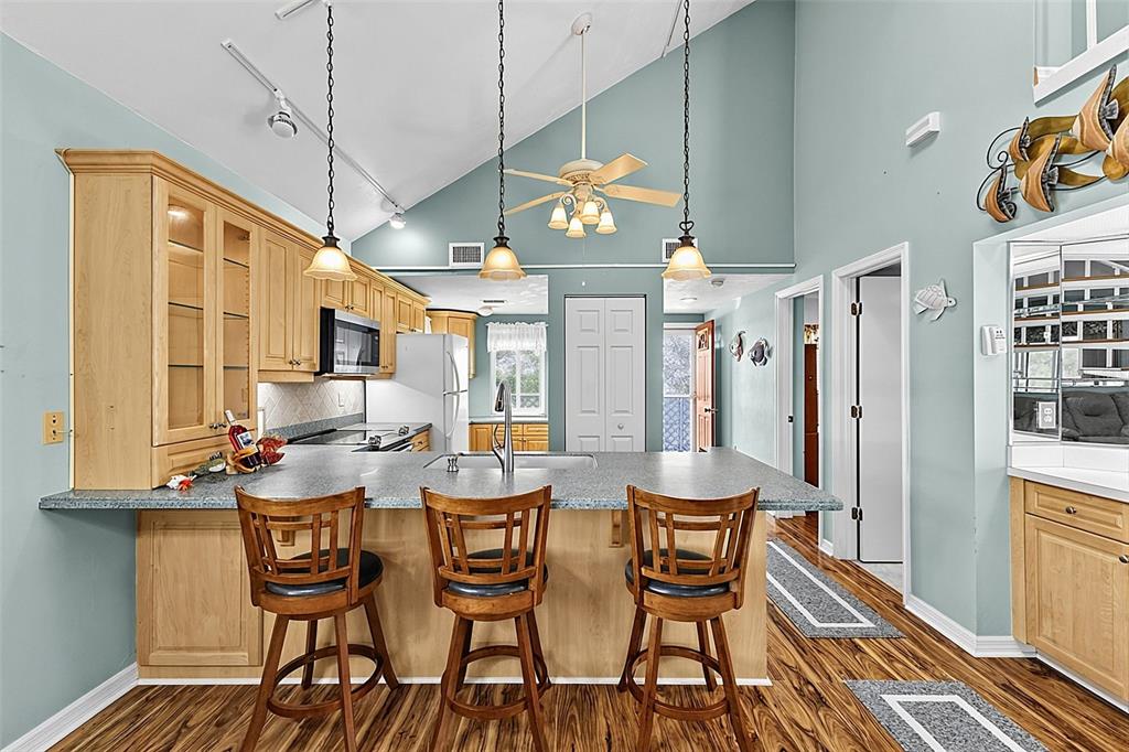 A kitchen with light wood cabinets, a gray countertop, and three bar stools — 6800 PLACIDA ROAD UNIT 281, ENGLEWOOD, FL