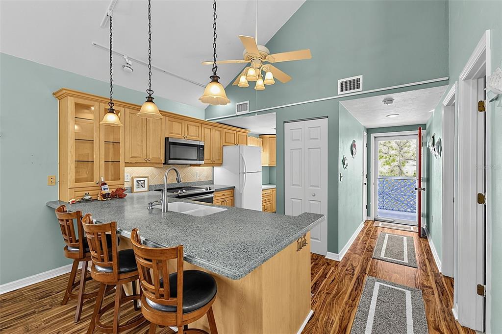 A kitchen features light wood cabinets, a granite-topped island with bar stools, and vaulted ceilings — 6800 PLACIDA ROAD UNIT 281, ENGLEWOOD, FL