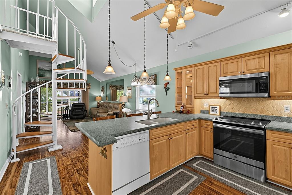 A kitchen with light wood cabinets, stainless steel appliances, and a white spiral staircase — 6800 PLACIDA ROAD UNIT 281, ENGLEWOOD, FL